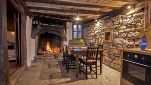 A stone-floored dining area with a fireplace, wooden ceiling beams, and a stone wall.