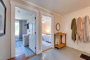 A hallway with a wooden door leading to a bedroom with a bed and a nightstand. There is a wall-mounted TV and a small wooden table with a basket. - Green Mountain Views! Lowell Getaway Near Skiing (Lowell)