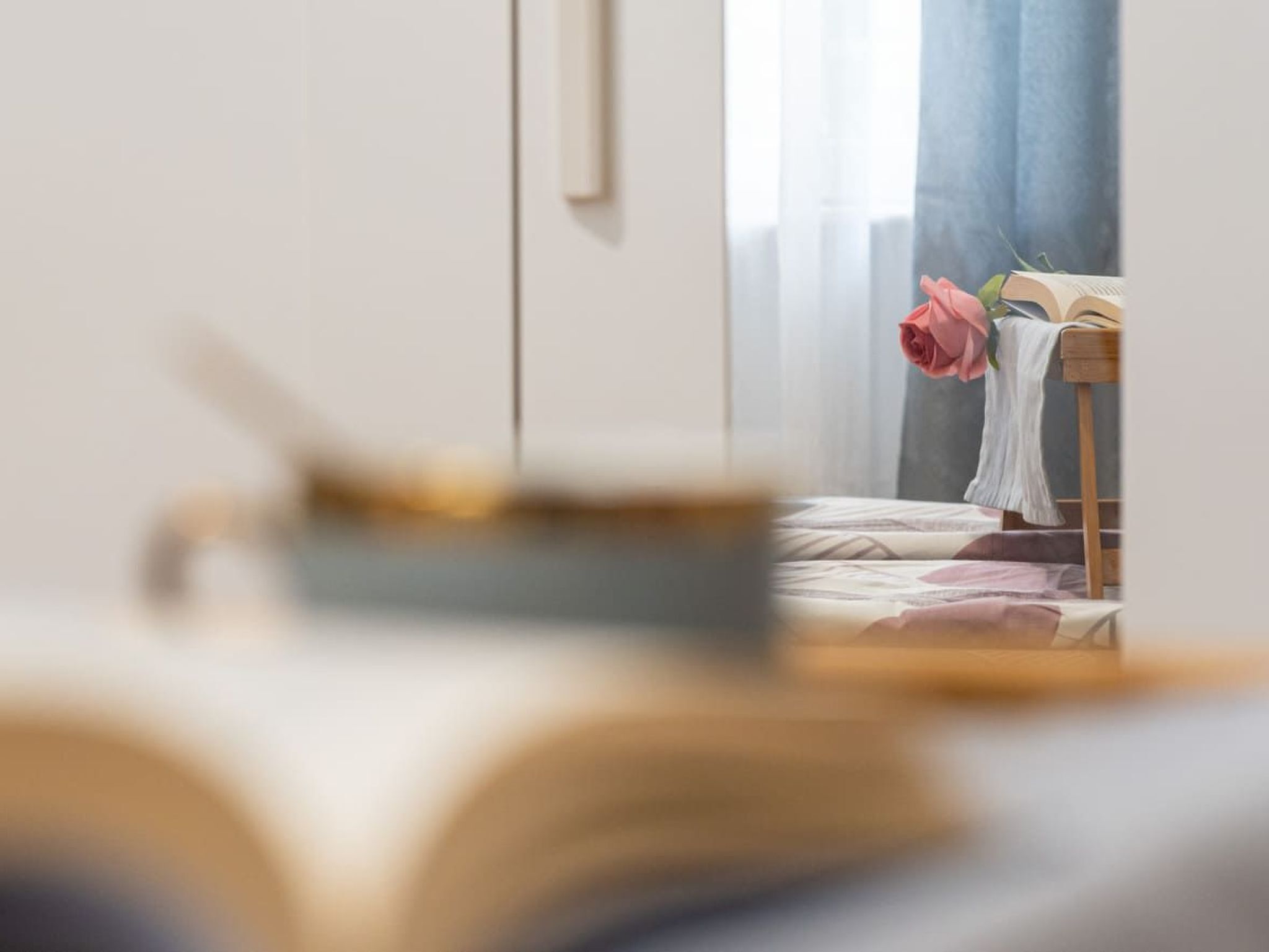 Makuuhuone, jossa on sänky, yöpöytä, jonka päällä on avoin kirja, ja vaaleanpunainen ruusu.