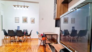 Ein modernes Wohnzimmer mit einem großen Flachbildfernseher, Holzboden und einem Essbereich mit Stühlen und Tisch.