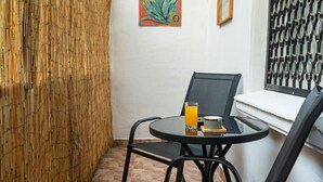 Ein kleiner, abgeschlossener Patio-Bereich mit einem runden Tisch und zwei Stühlen, einem Glas Orangensaft und einem gerahmten Bild an der Wand.
