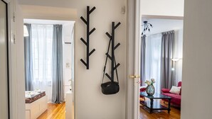 Ein Flur mit einer Bank, einem Kleiderständer mit einer Tasche und einem Blick in ein Wohnzimmer mit einem roten Sofa und einer Lampe.