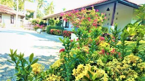 A residential area with a house featuring a tiled roof and a well-maintained garden with various flowering plants.