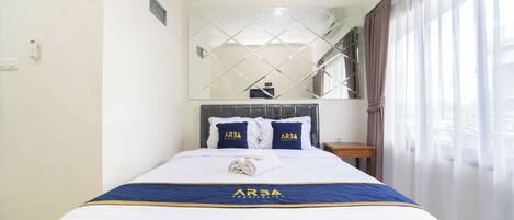 A hotel room with a neatly made bed, a large mirror above the bed, and a view of a staircase.