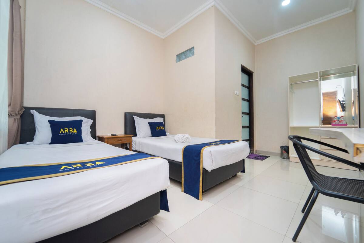 Une chambre d’hôtel avec deux lits, chacun recouvert d’une courtepointe bleue et blanche et agrémenté d’oreillers, un bureau avec une chaise et un miroir au-dessus du bureau.