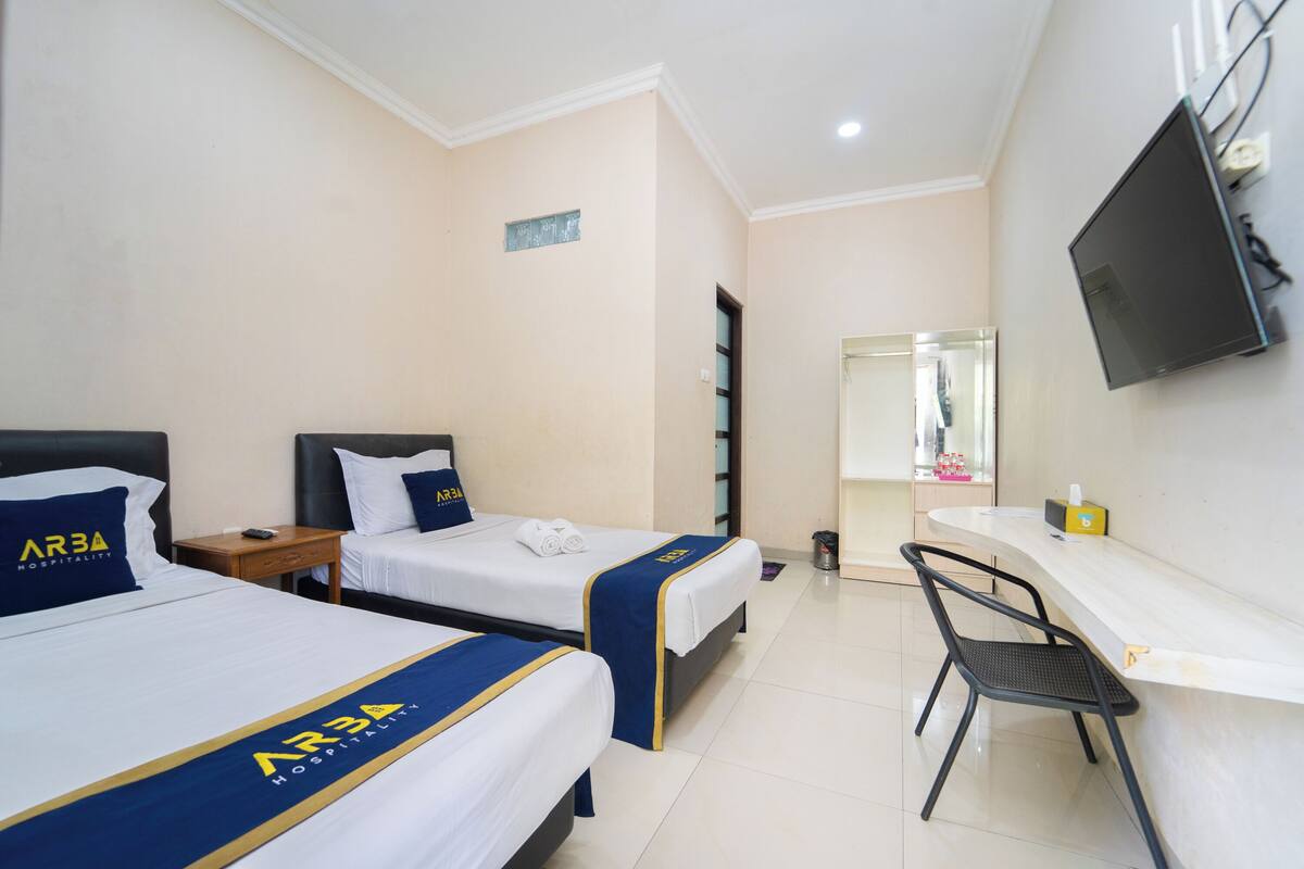 Une chambre d’hôtel avec deux lits, un bureau, une chaise et un téléviseur fixé au mur.