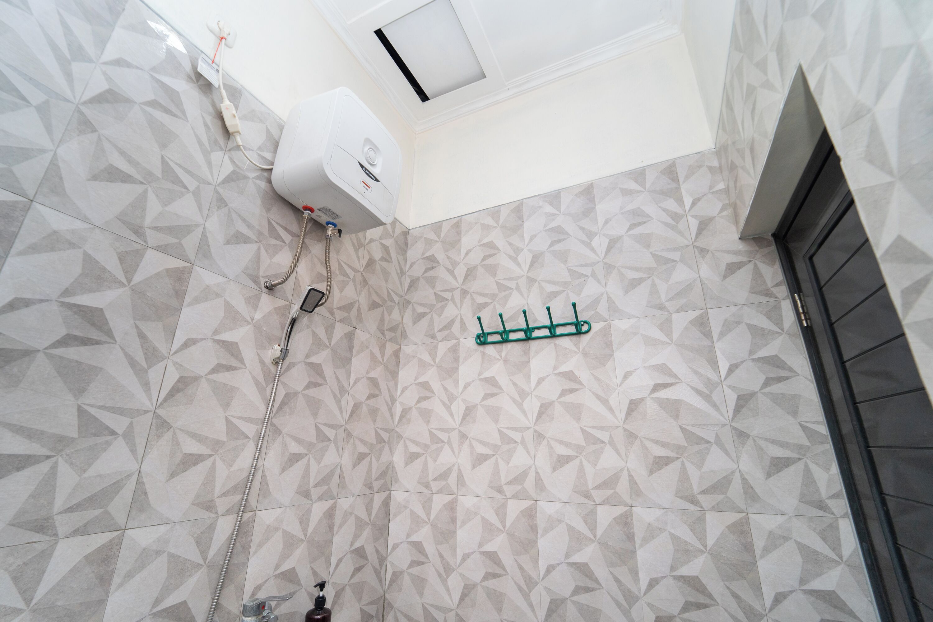 Ein Badezimmer mit geometrisch gemusterten Fliesen, einer unter der Decke montierten Klimaanlage und einem grünen Handtuchhalter.