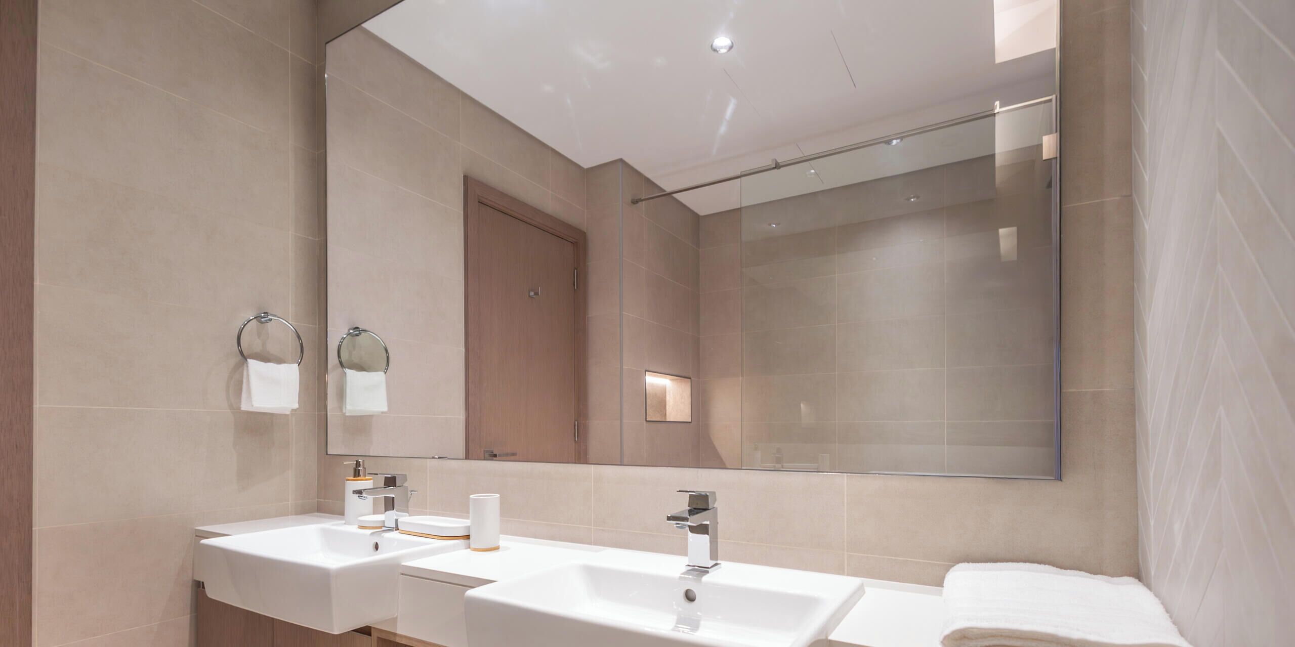 A modern bathroom with two sinks, a large mirror, and a shower area.