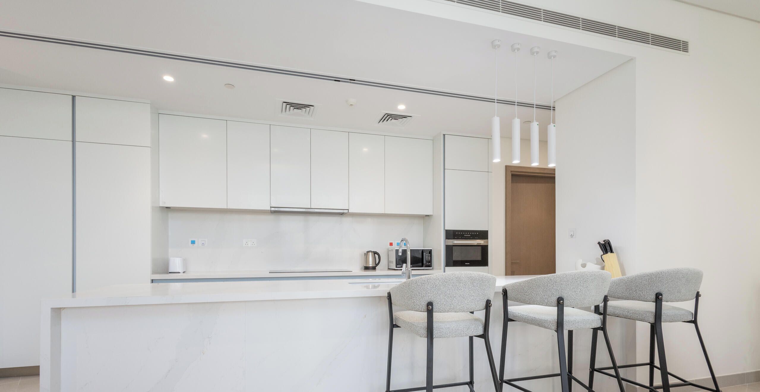 A modern kitchen with white cabinets, a central island with bar stools, and a microwave.