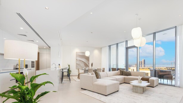 Una sala moderna con un sofá grande, una mesa de centro y vistas de la ciudad a través de amplias ventanas.
