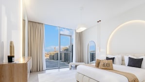 Habitación de hotel moderna con una cama grande, un escritorio y vistas a la ciudad a través de ventanales de piso a techo.