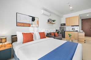 A modern hotel room with a large bed, a desk, a sofa, a kitchen area, and a dining table. - Hesrin by Kozystay - Sentul (Bogor)