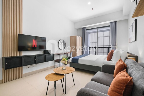 A modern hotel room with a bed, sofa, TV, and a small table with a vase of flowers. - Hesrin by Kozystay - Sentul (Bogor)