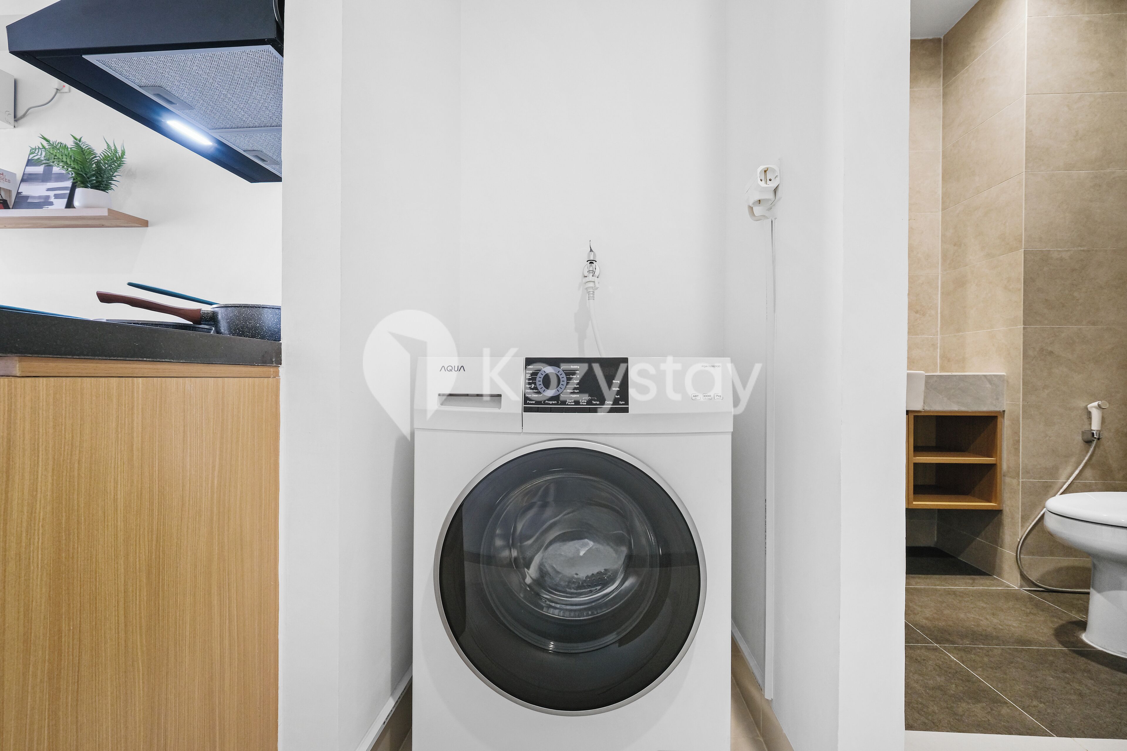 A compact laundry room with a front-loading washing machine, a small shelf with a plant, and a visible water heater.