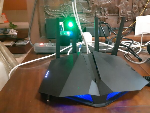 A router on a desk with multiple cables and a green light indicator.