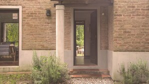 A brick building with a tiled roof entrance, a visible door, and a small outdoor seating area with a table and chairs. - Cozy 2-bedroom house in El Tesoro with AC (El Tesoro)