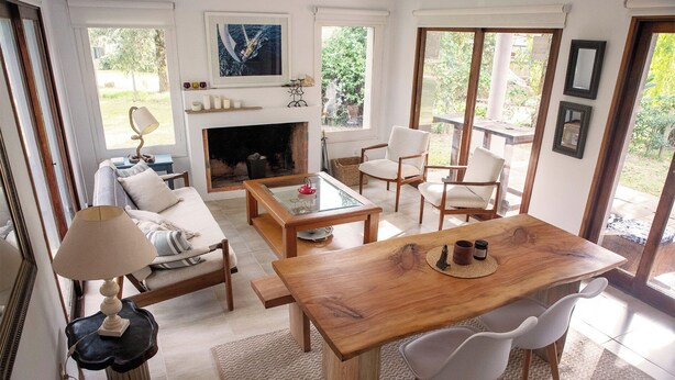 A spacious living room with a fireplace, a dining area with a wooden table and chairs, and a cozy seating area with a sofa and armchairs. - Cozy 2-bedroom house in El Tesoro with AC (El Tesoro)