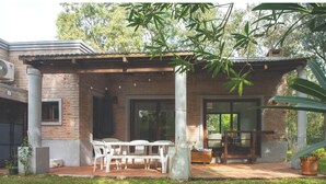 A covered outdoor patio with a brick wall, white plastic chairs, and a table. - Cozy 2-bedroom house in El Tesoro with AC (El Tesoro)