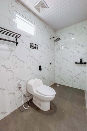 A bathroom with a white toilet, marble-patterned walls, a showerhead, and a towel rack. - Golden House Syariah Nexura Collection (Dieng Kulon)