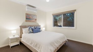A bedroom with a bed, a nightstand, a lamp, an air conditioner, a window, and a painting on the wall. - Incredible Elevated Views Pet Friendly (Ocean Grove)
