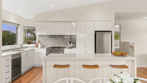 A modern kitchen with white cabinetry, a central island with stools, a built-in oven, and a stainless steel refrigerator. - Incredible Elevated Views Pet Friendly (Ocean Grove)