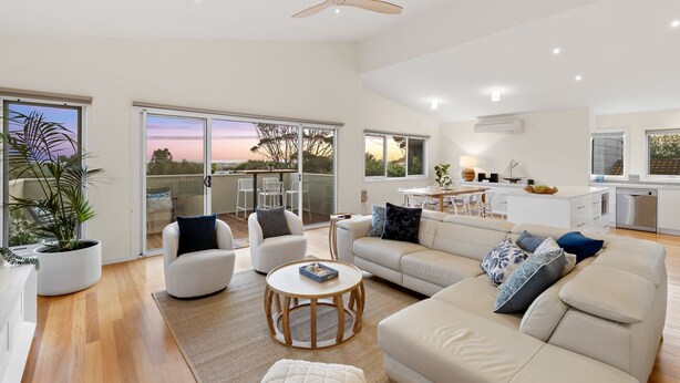 A spacious living room with a large sofa, a coffee table, and a ceiling fan. There is a sliding glass door leading to a balcony with outdoor furniture. - Incredible Elevated Views Pet Friendly (Ocean Grove)