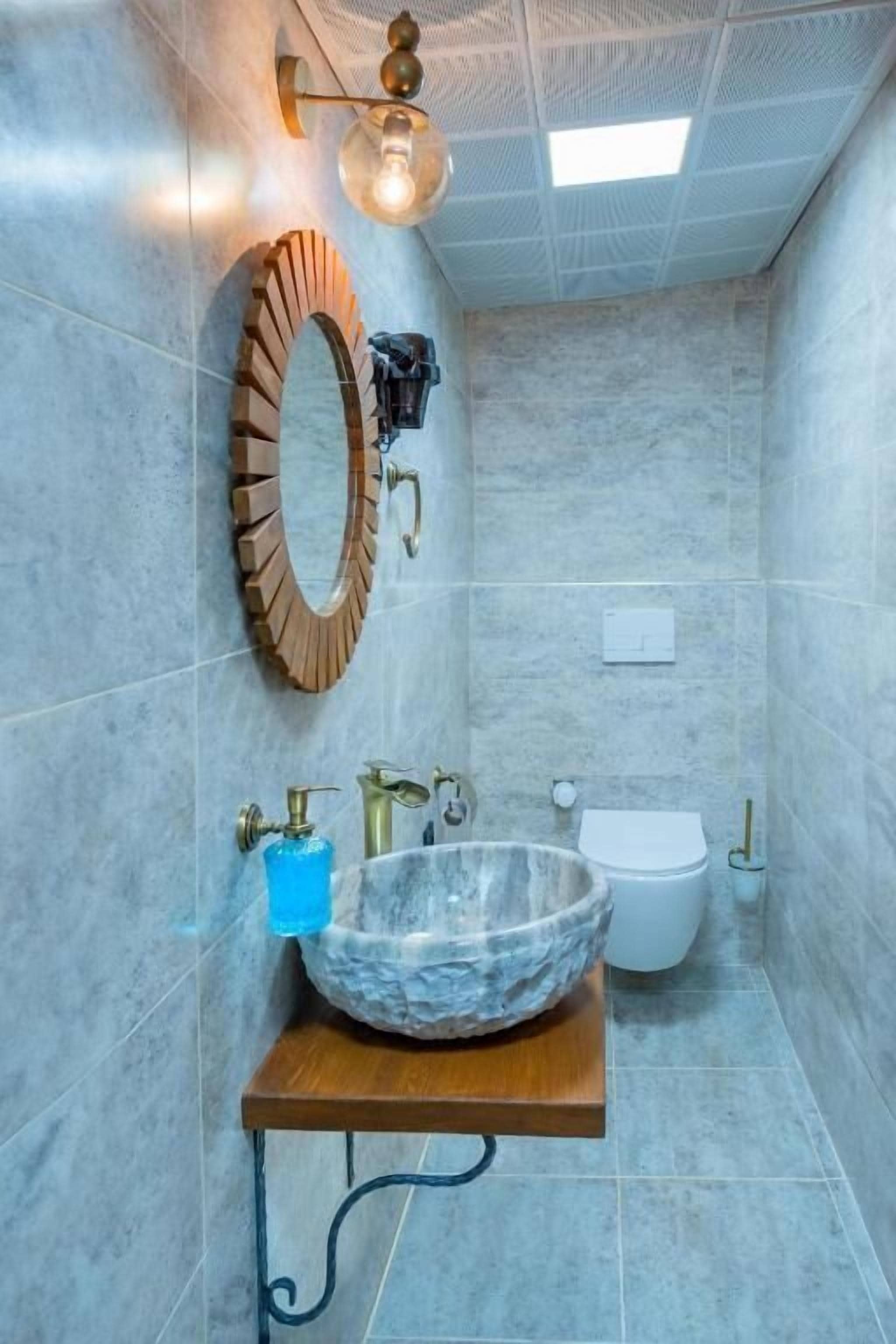 A bathroom with a marble sink, a wooden vanity, a white toilet, and a wall-mounted mirror.