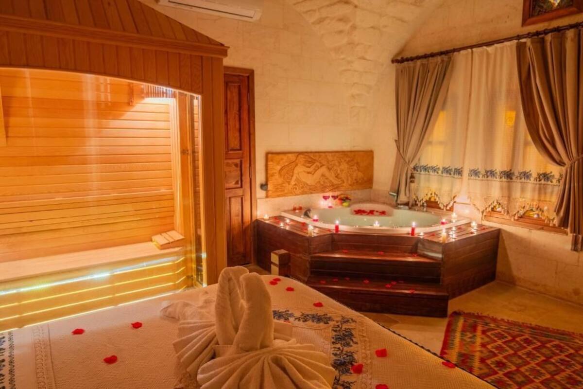 Um quarto de spa com piso de madeira, mesa de massagem com pétalas de rosa, cabeceira de madeira e banheira com velas.