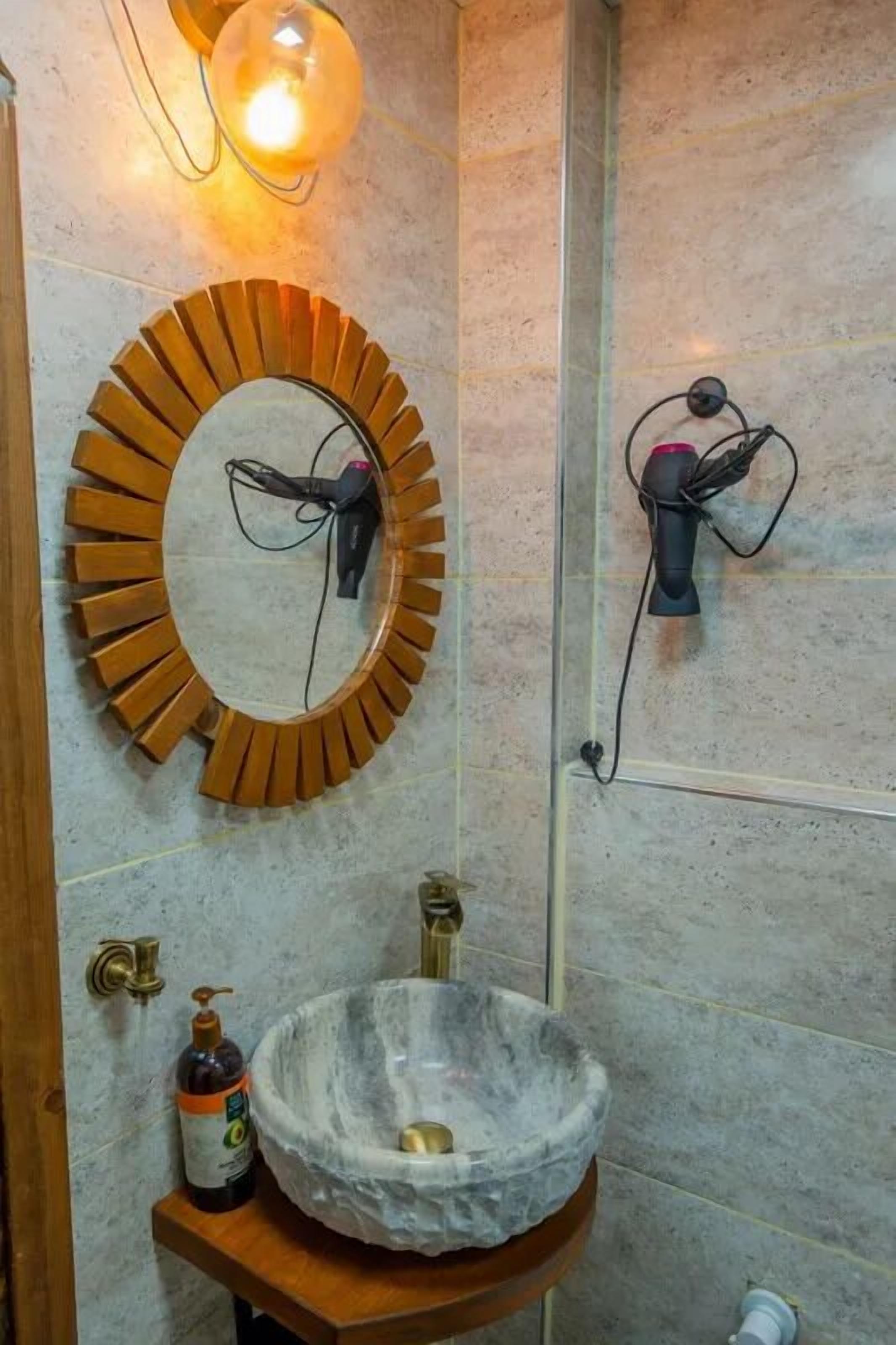 A bathroom with a round mirror, a marble sink, and two wall-mounted hair dryers.