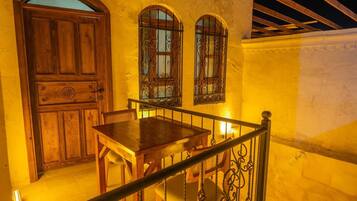 A wooden table and chairs set against a yellow wall with two arched windows with metal bars.