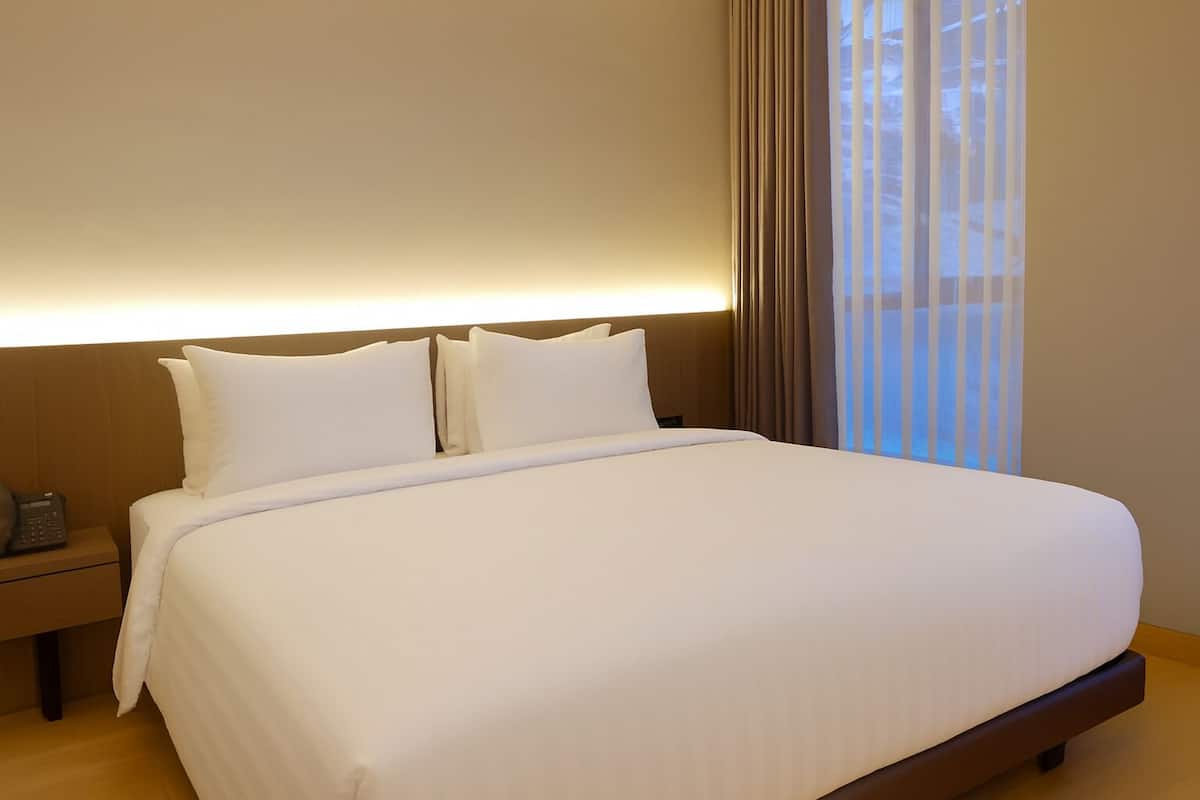 A hotel room with a large bed, a bedside table with a phone, and a window with curtains.