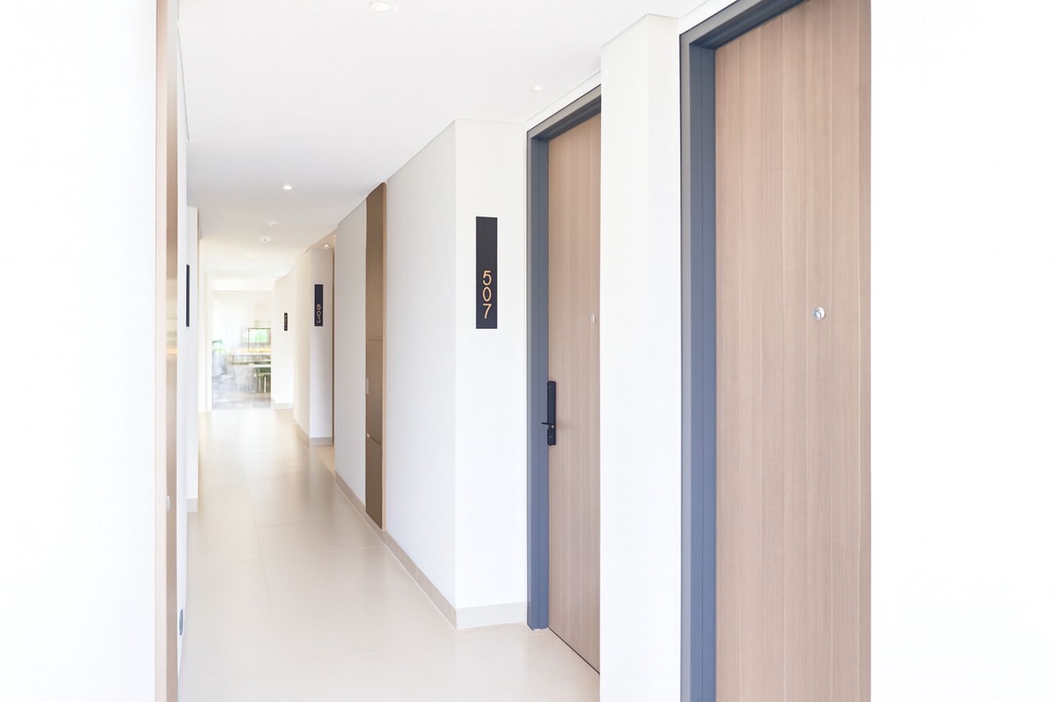 Un pasillo moderno de hotel con puertas de madera, placas de identificación de habitaciones numeradas y un piso de baldosas limpias.