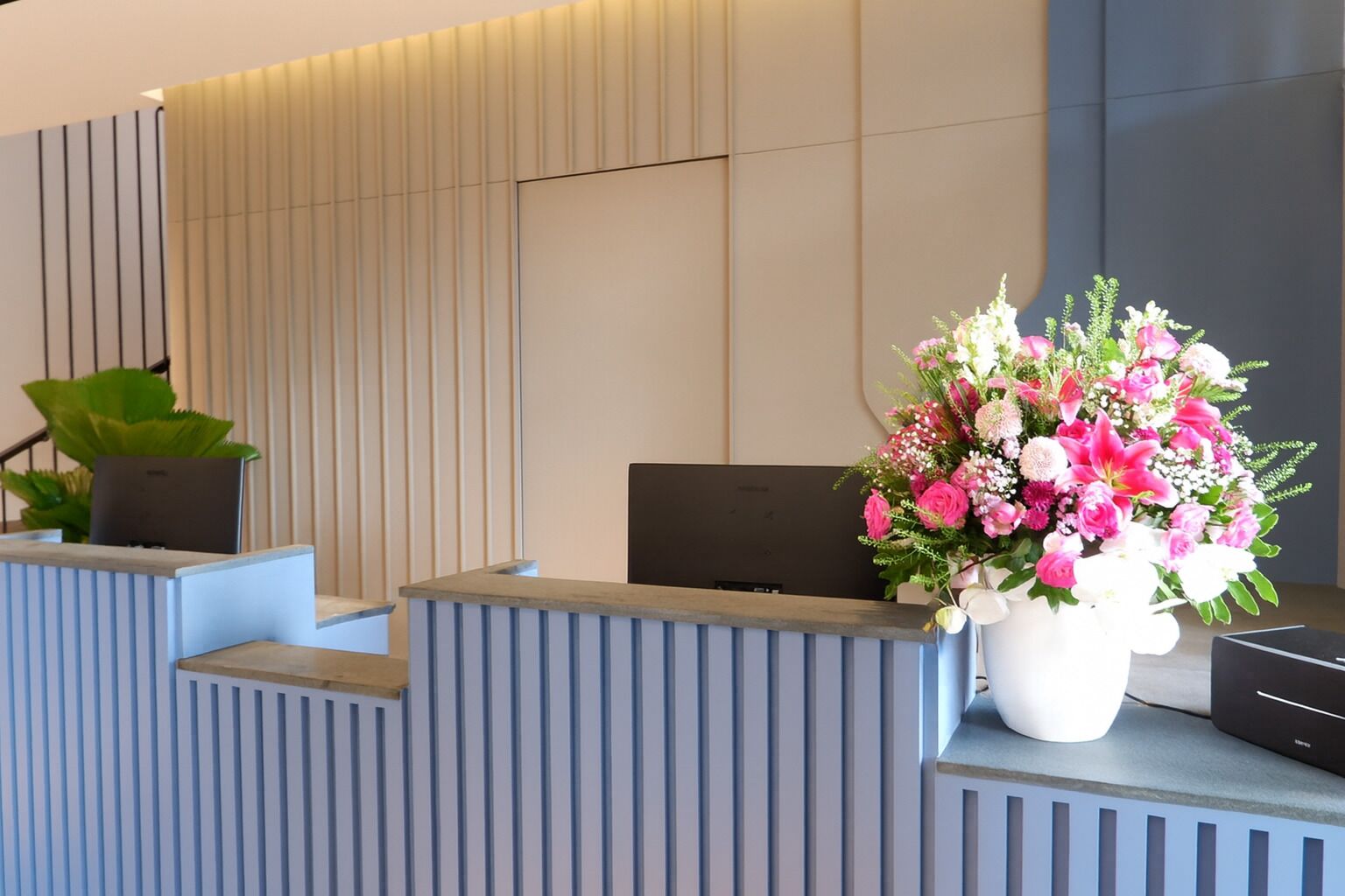 A reception desk with a modern design, featuring vertical lines and a large floral arrangement.