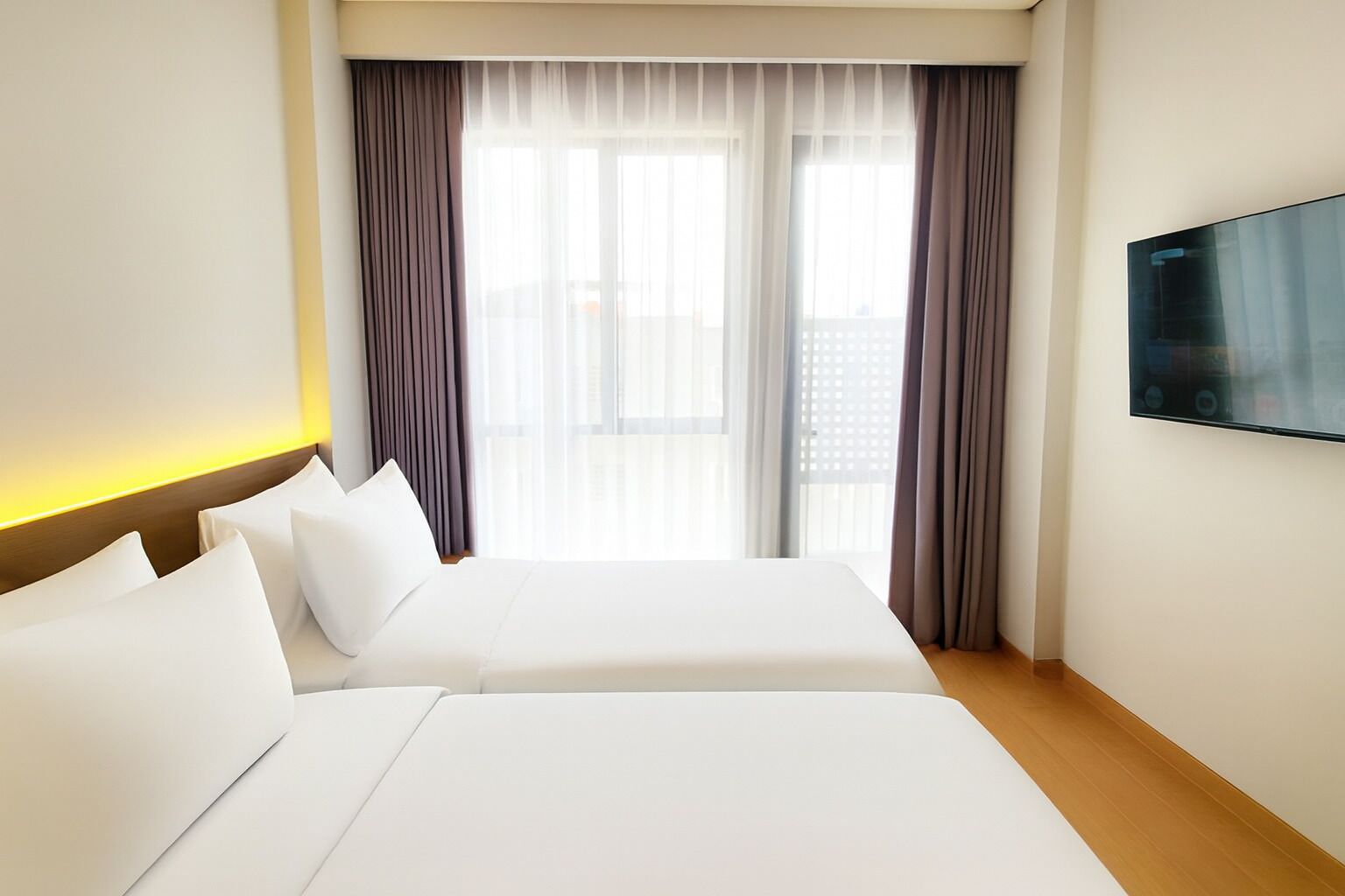 Habitación de hotel con dos camas, un televisor montado en la pared y un balcón con cortinas.