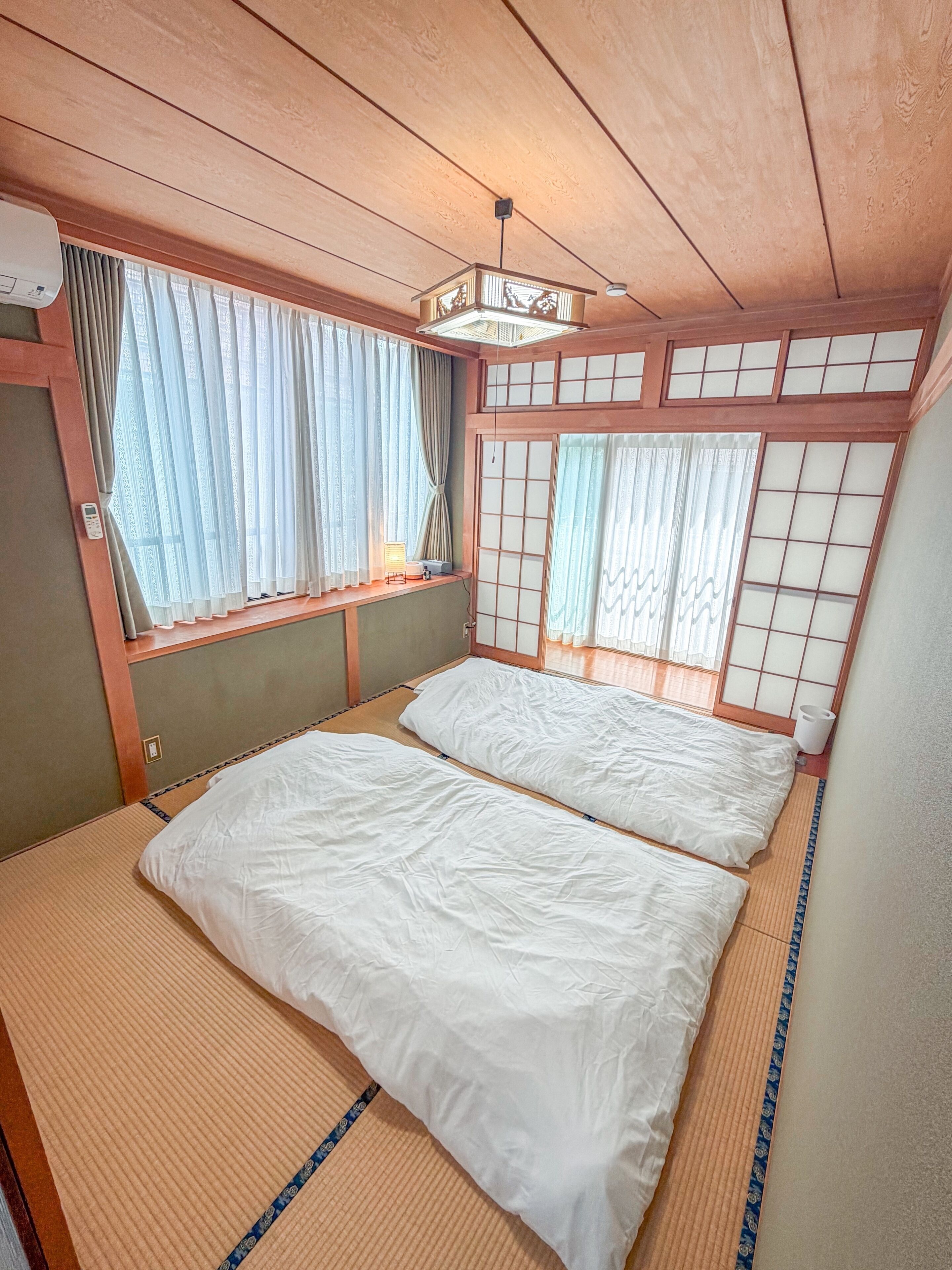 A traditional Japanese-style room with tatami flooring, a futon bed, sliding shoji doors, and a ceiling fan.