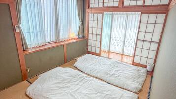 A traditional Japanese-style room with tatami flooring, a futon bed, sliding shoji doors, and a ceiling fan.