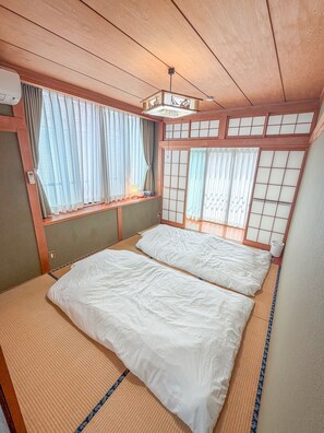 Una habitación tradicional japonesa con suelo de tatami, futón, puertas correderas shoji y un ventilador de techo.