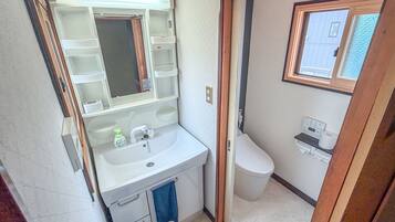 A compact bathroom with a sink, mirror, toilet, and a window.