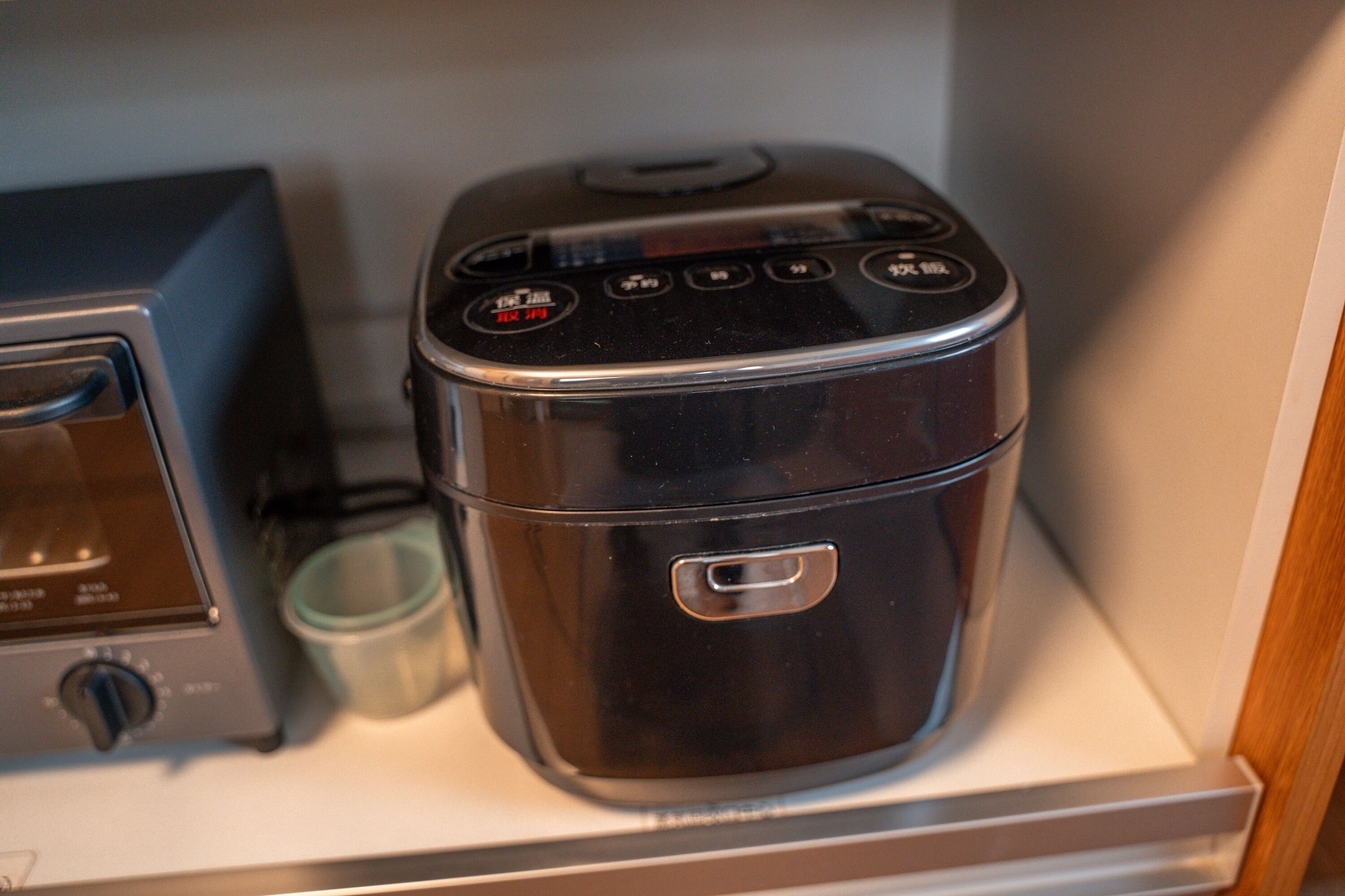 Une petite cuisine équipée d’un four à micro-ondes et d’un cuiseur à riz, le tout placé sur une étagère.