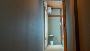 Een gang met houten vloer, een plafondlamp en een deur naar een andere kamer.