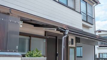 Ein zweistöckiges Wohngebäude mit Balkon, geschlossenem Eingangstor und einem kleinen Garten.