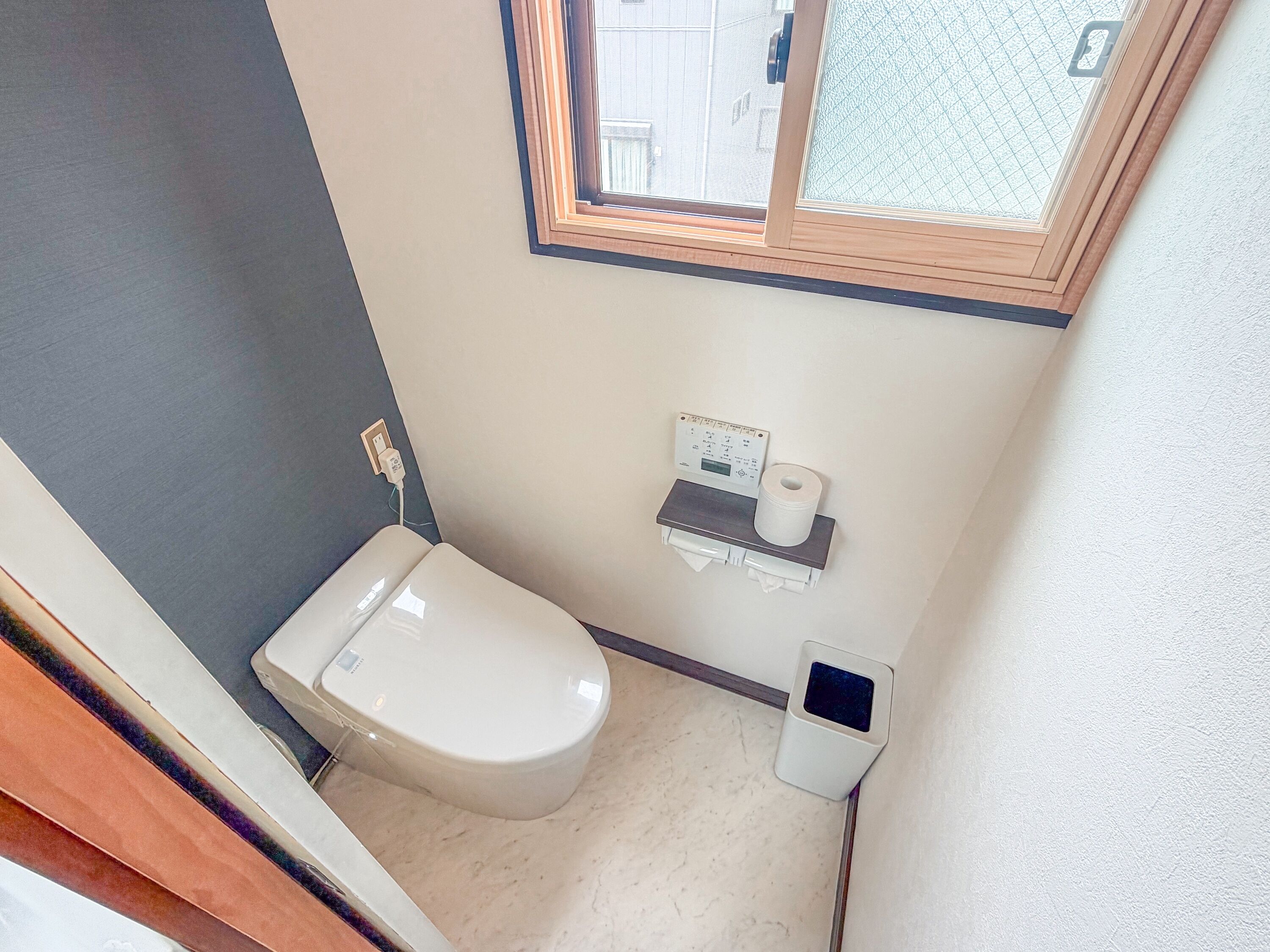 A small, compact bathroom with a toilet, a hand dryer, a paper towel dispenser, and a window above the toilet.