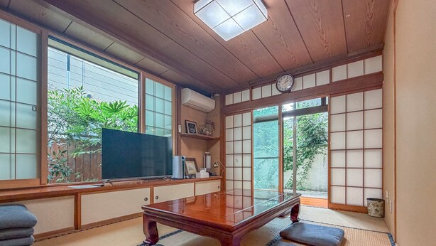 Een kamer met tatami matten, een houten tafel, kussens, een televisie en een klok.