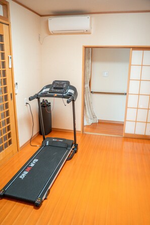 Habitación con caminadora, aire acondicionado de pared, piso de madera y puerta corrediza.