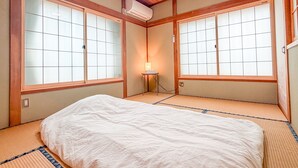 Een traditionele Japanse kamer met tatami vloeren, een bed, schuifdeuren en een plafondventilator.