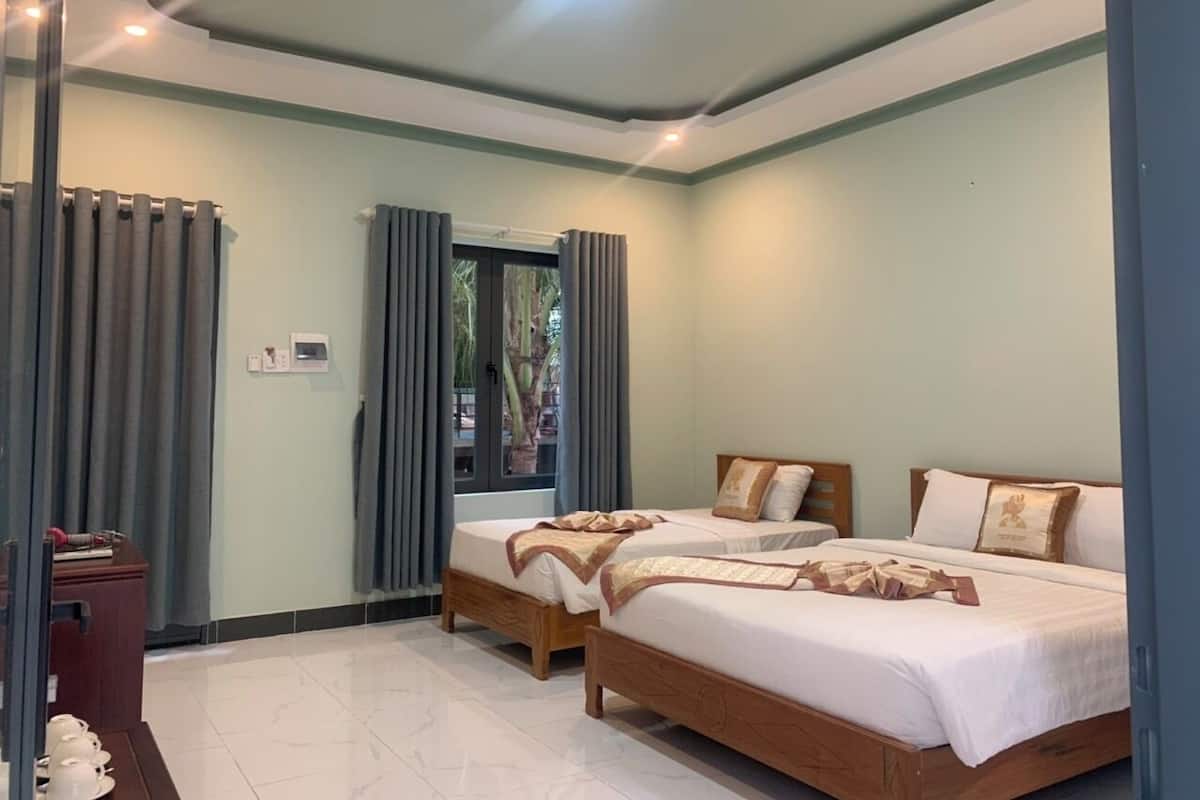 A hotel room with two beds, a wooden nightstand, and a window with curtains.