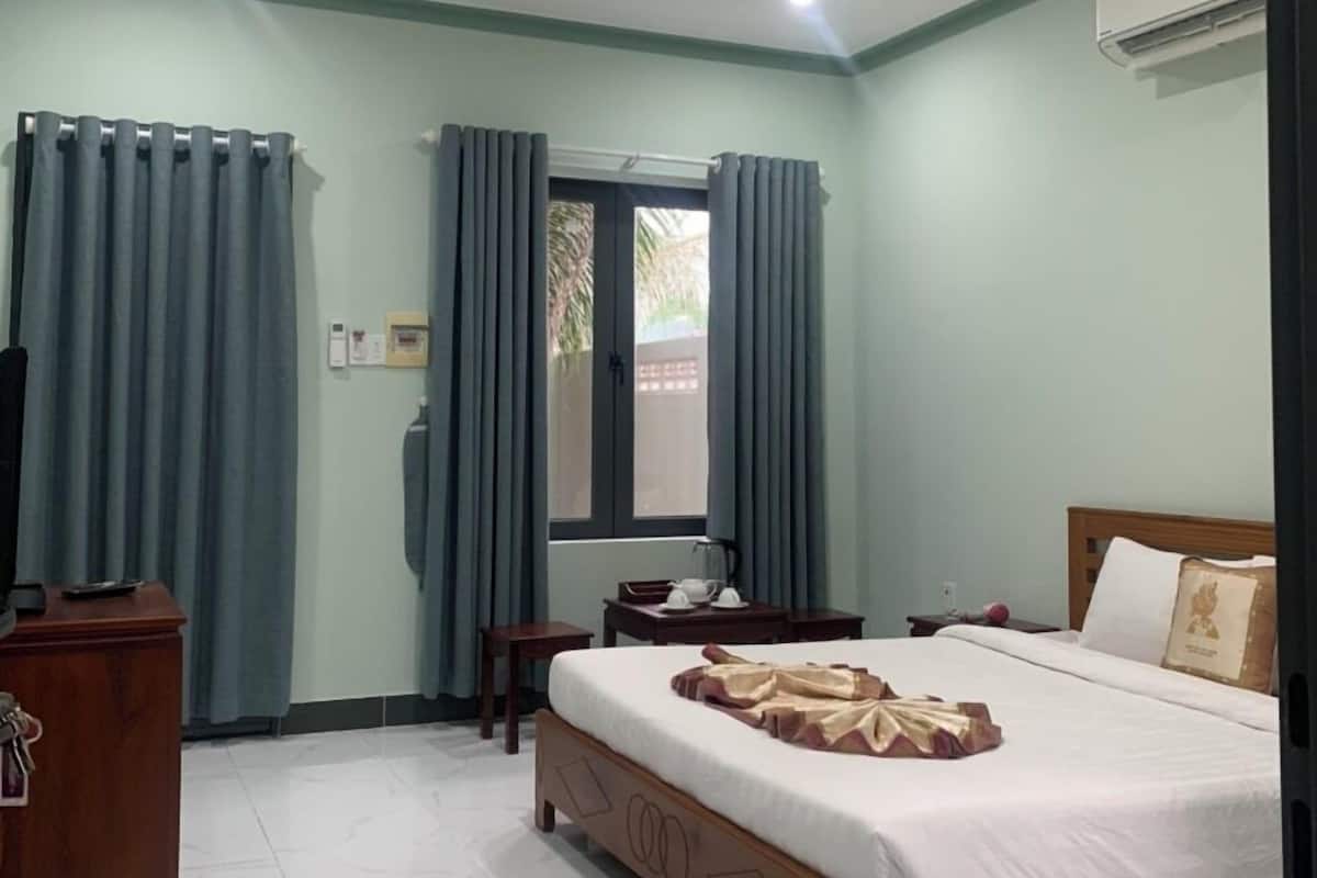 A hotel room with a bed, a desk, a chair, a television, and a window with curtains.