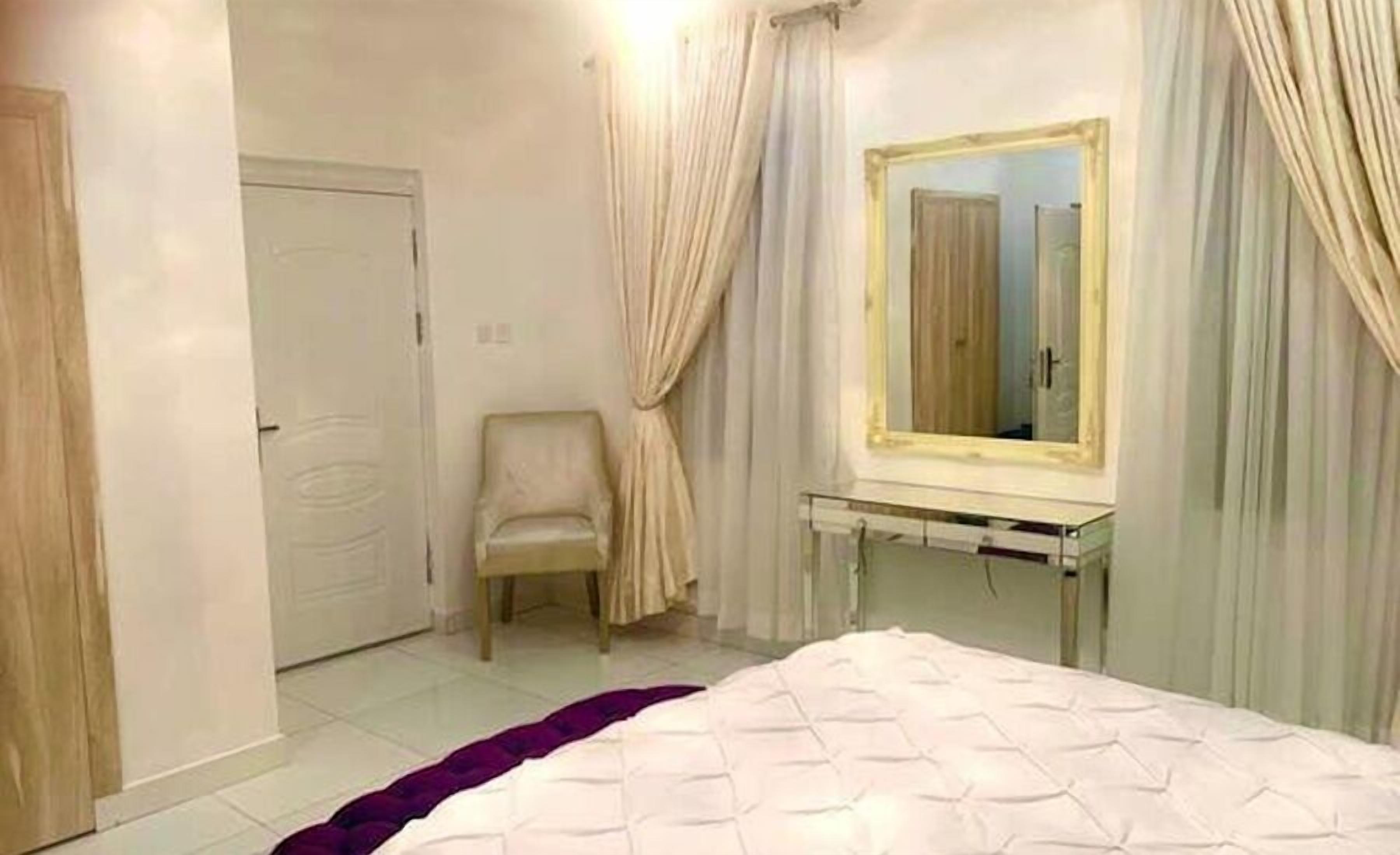 A bedroom with a bed, a chair, a vanity with a mirror, and curtains.