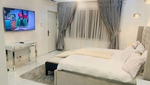 Quarto com cama, televisão, mesa de cabeceira e cortinas.