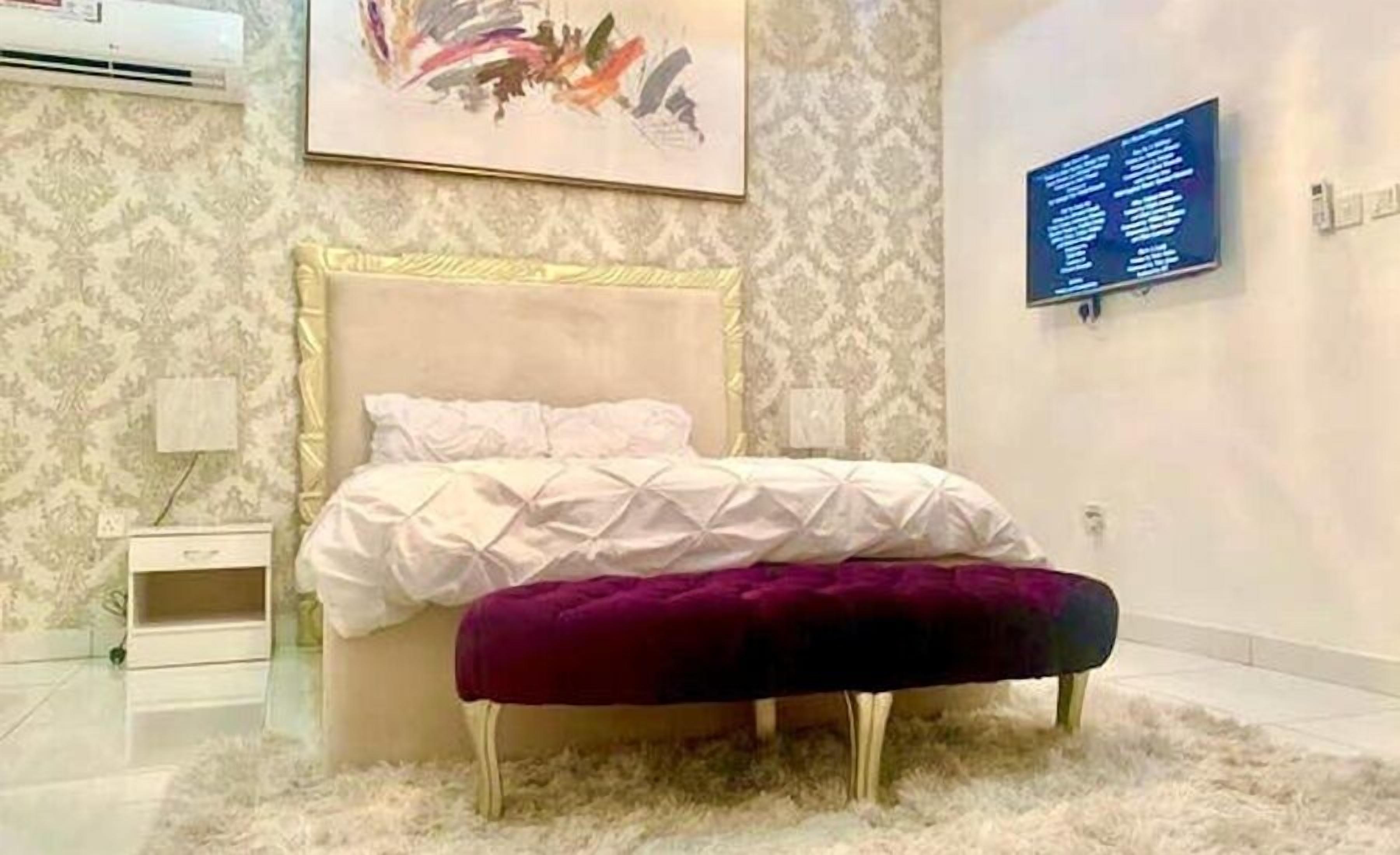 A bedroom with a bed, a nightstand, a wall-mounted TV, and a decorative painting.